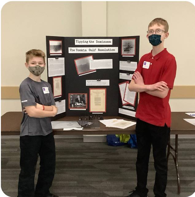 Two students standing in front of their history exhibit with their arms crossed in front of them